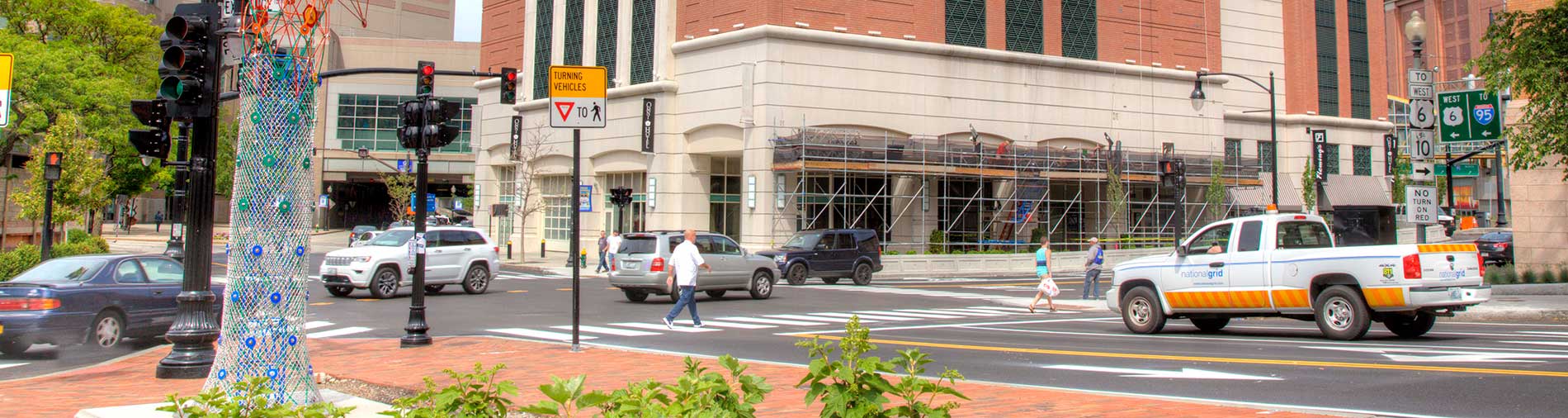 Photo of downtown Providence intersetion, with moving and stopped traffic. Pedestrians are crossing the street at crosswalks.