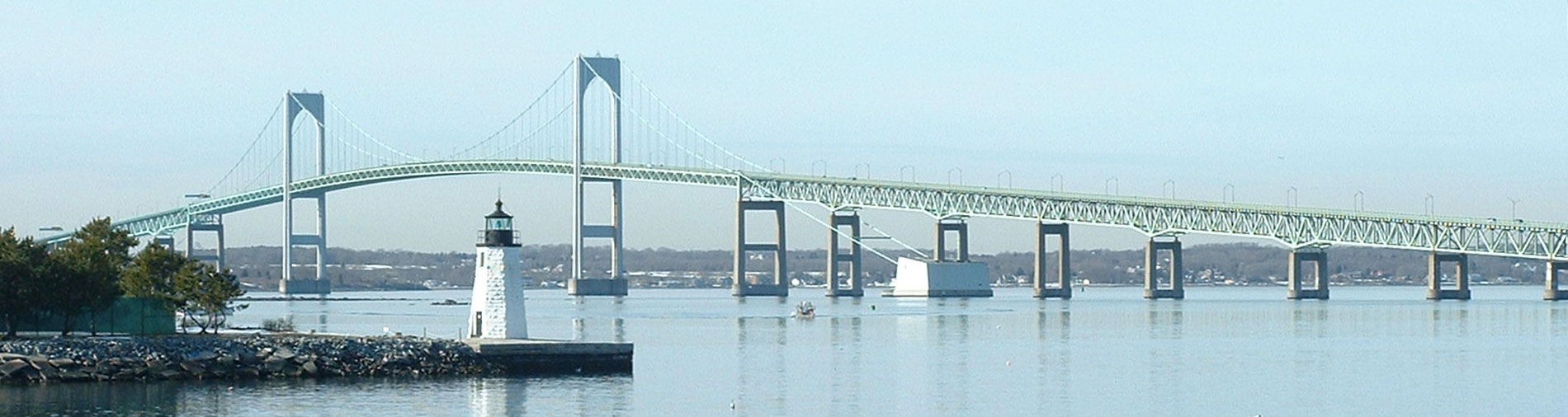 Photo of Narragansett Bay and Clairborne Pell (Newport) Bridge in the distance. The sky is clear and the water calm.